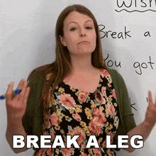 a woman in a floral dress stands in front of a white board with the words break a leg written on it