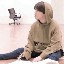 a person wearing a hoodie sits on the floor with a pen in their hand