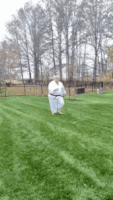 a man in a white karate uniform is running on a lush green lawn .