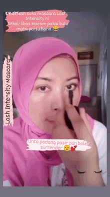 a woman in a pink hijab is applying mascara to her eyelashes