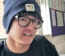 a man wearing glasses and a beanie with the letter k on the label