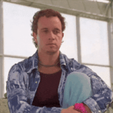 a man sitting in front of a window wearing a blue and white shirt
