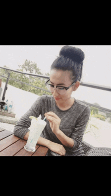 a woman wearing glasses is sitting at a table with a drink