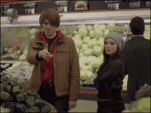 a man and a woman are standing in a grocery store with a sign that says ' vegetables ' on it