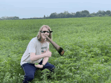 a man wearing sunglasses and a nasa shirt is kneeling in a field of plants