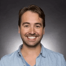 a man with a beard is wearing a blue shirt and smiling for the camera .