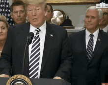 a man in a suit and tie stands behind a podium with the seal of the president of the united states on it