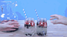 two people toasting with mason jars filled with strawberries and blueberries with a pitcher in the background that says country living