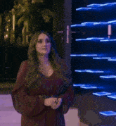 a woman in a red dress and black belt is standing in front of a wall of lights .