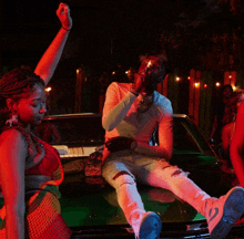 a man is sitting on the hood of a green car