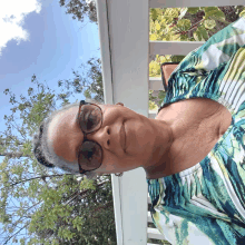 a woman wearing glasses and a green and white top is standing on a balcony