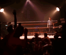 a referee stands in the middle of a boxing ring with a crowd watching