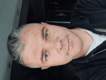 a man with gray hair and blue eyes is wearing a black jacket and white shirt