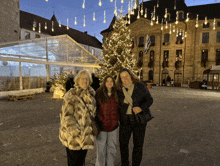 three women are posing for a picture in front of a christmas tree