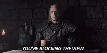 a man in armor is sitting at a table and says you 're blocking the view .