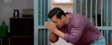 a man in a purple shirt is kneeling down with his hands folded in prayer .