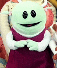 a green stuffed animal wearing a purple dress and white sleeves