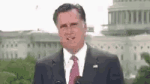 a man in a suit and tie is standing in front of a microphone in front of a capitol building .