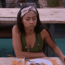 a woman wearing a headband is sitting at a table with a plate of food and a glass of water