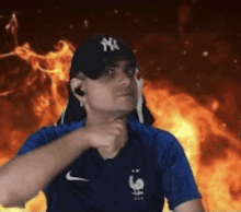 a man wearing a new york yankees hat and a blue shirt is standing in front of a fire .