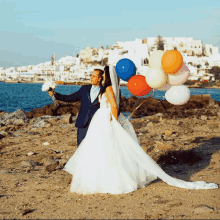 a bride and groom hold a bunch of balloons in front of the ocean