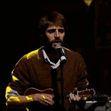 a man singing into a microphone while holding a guitar in front of a sign that says television de catalunya