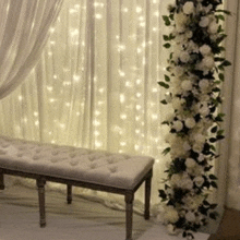 a white bench is sitting in front of a window with a floral arrangement .