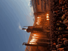 a crowd of people watching a concert with flames coming out of a stage