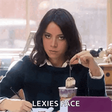 a woman is sitting at a table with a tea bag in her hand and the words lexies face written on the screen .