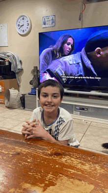 a young boy sits at a table in front of a television screen that says i think you better get up to the fire floor