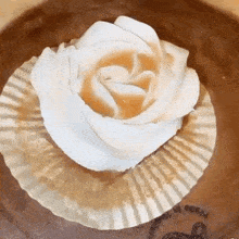 a close up of a cupcake with whipped cream in the shape of a rose on a paper wrapper .