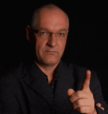 a man wearing glasses and a suit points his finger