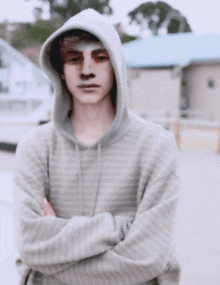 a young man wearing a striped hoodie stands with his arms crossed in front of a building