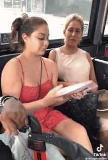 two women are sitting on a bus and one of them is holding a book