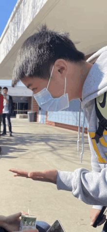 a young man wearing a face mask holds out his hand