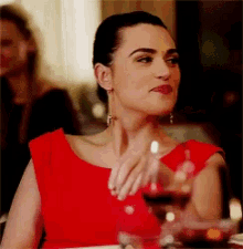 a woman in a red dress is sitting at a table drinking a glass of wine .