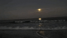 a full moon is shining over the ocean at night