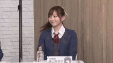 a girl in a school uniform sits at a table with a bottle of water and a sign with chinese writing