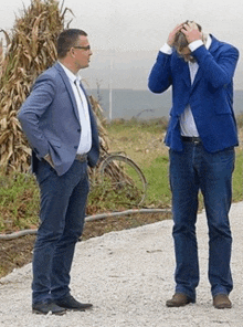 a man in a blue jacket has his hands on his head while standing next to another man