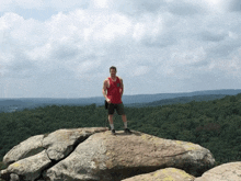 a man in a red tank top is standing on a rock