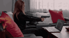 a woman sits on a couch holding a gun in front of a laptop