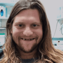 a man with long hair and a beard is smiling with a missing tooth