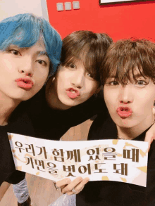 three young men are posing for a picture and one of them is holding a sign with korean writing