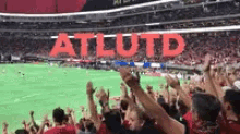 a crowd of people are standing in a stadium with their arms in the air and a sign that says atl utd