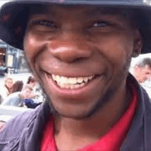 a man wearing a hat and a red shirt is smiling and looking at the camera .