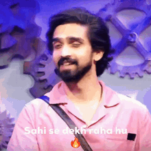 a man with a beard is wearing a pink shirt with the words sahi se dekh raha hu on it .