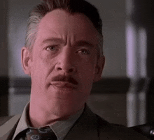 a man with a mustache is wearing a suit and tie and making a funny face .