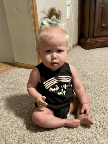 a baby wearing a tank top that says good vibes only sits on the floor