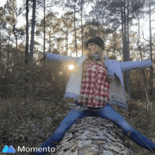 a woman in a plaid shirt is sitting on a log in the woods with the momento logo in the corner