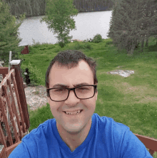 a man wearing glasses and a blue shirt takes a selfie in front of a lake